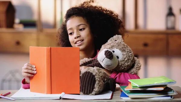 Glücklich afrikanisch-amerikanisches Kind liest Buch zu Teddybär — Stockfoto