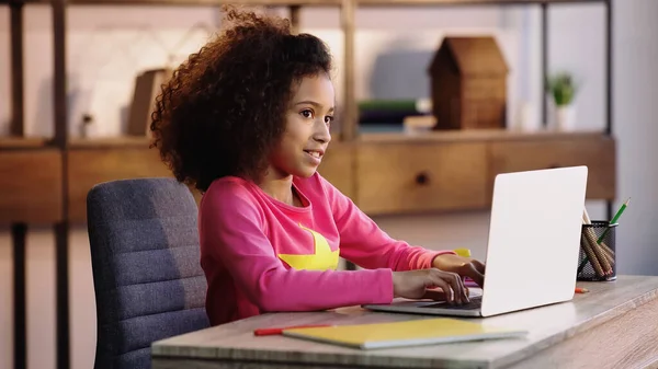 Fröhliche afrikanisch-amerikanische Schulkind mit Laptop bei den Hausaufgaben — Stockfoto