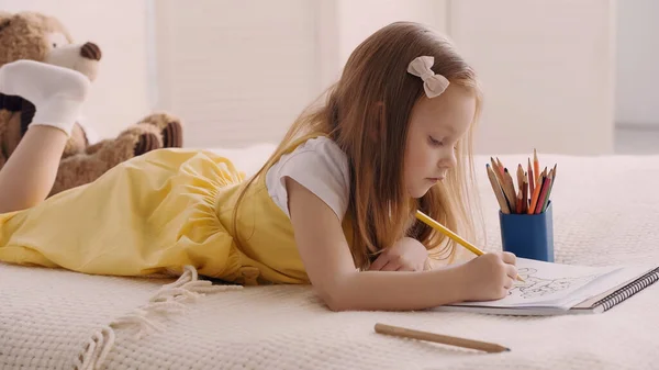 Preschooler child drawing while lying on bed — Stockfoto