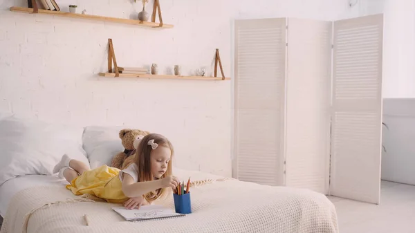 Kind nimmt Farbstift in der Nähe von Papier auf dem Bett zu Hause — Stockfoto