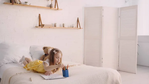 Kid taking color pencil near paper on bed at home — Stock Photo