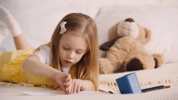 Child drawing near paper and color pencils on bed at home — Stock Photo