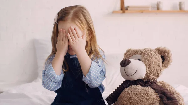 Child covering face with hands near soft toy in bedroom — Stock Photo