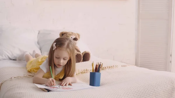 Bambino disegno mentre sdraiato sul letto vicino peluche in camera da letto — Foto stock