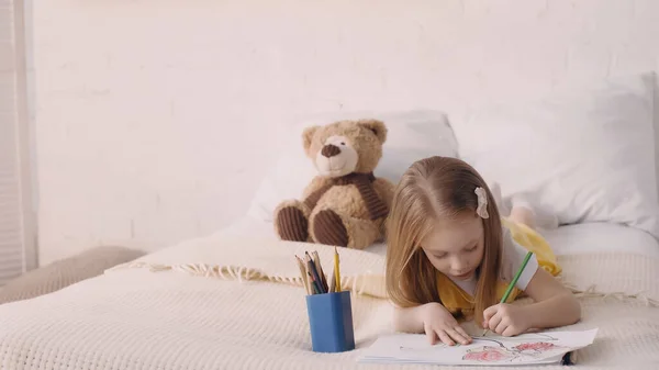 Girl drawing on paper near color pencils in bedroom — Foto stock