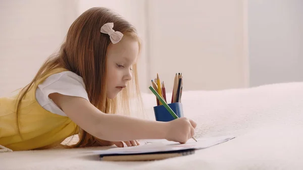 Kid drawing on paper while lying on blanket on bed — Stock Photo