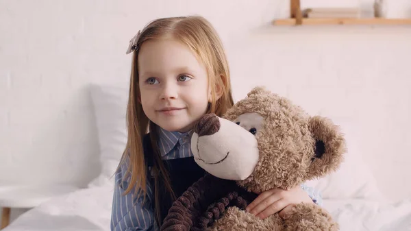 Smiling kid hugging teddy bear in bedroom — Stock Photo