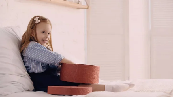 Alegre niño sosteniendo caja de regalo en la cama en casa - foto de stock