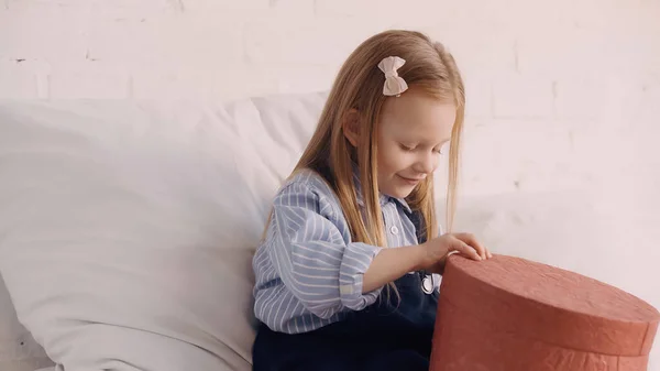 Smiling girl holding present on bed at home — Stock Photo