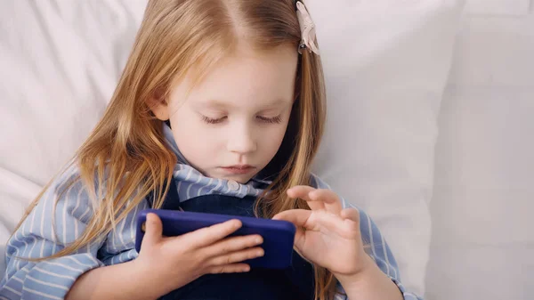 Child using mobile phone on bed at home — Stock Photo