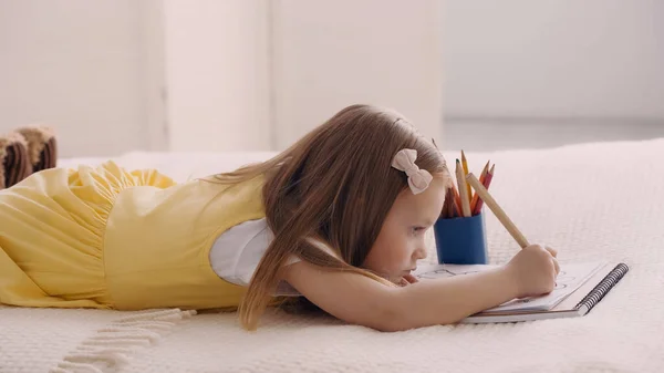 Side view of kid drawing on paper while lying on bed — Stock Photo