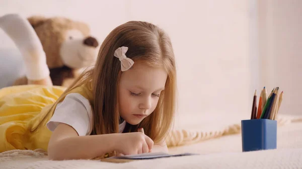 Child drawing near color pencils in bedroom — Stock Photo