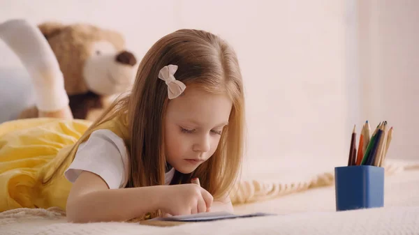 Child drawing near color pencils in bedroom — Stockfoto