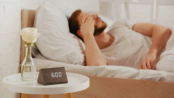 Clock and flower near sleepy man on bed at home — Fotografia de Stock