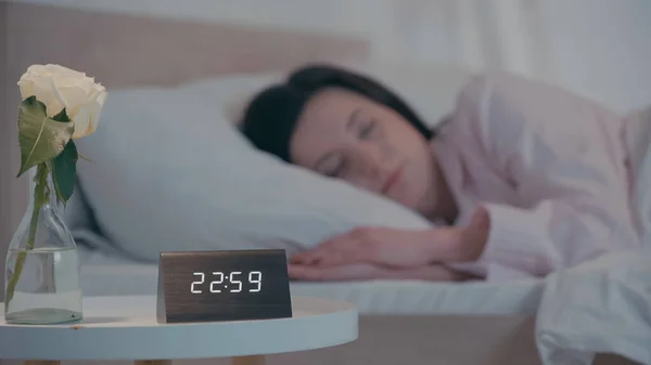 Flower and clock on bedside table near blurred woman sleeping at home — Stockfoto