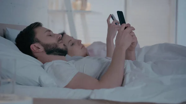 Junges Paar nutzt Smartphone zu Hause im Bett — Stockfoto