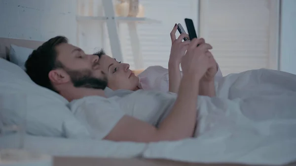 Young woman using smartphone near husband on bed at home — Foto stock