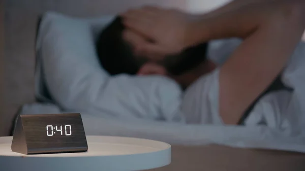 Clock on bedside table near blurred man on bed at night — Stockfoto