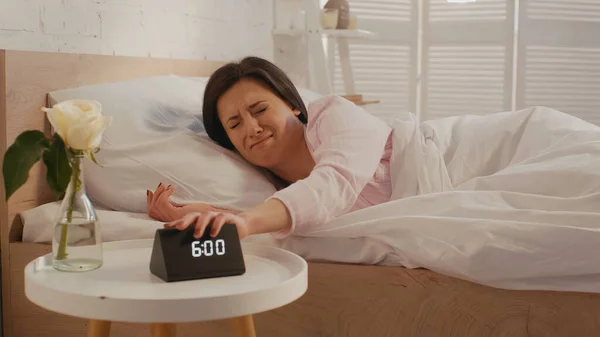 Dissatisfied woman turning off clock near plant on bedside table in bedroom — Stockfoto