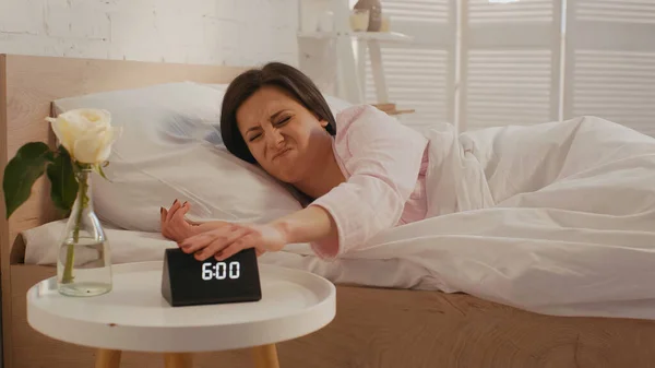 Mujer decepcionada apagando el reloj en el dormitorio por la mañana - foto de stock