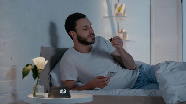 Giovane uomo guardando la barretta di cioccolato sul letto di notte — Foto stock