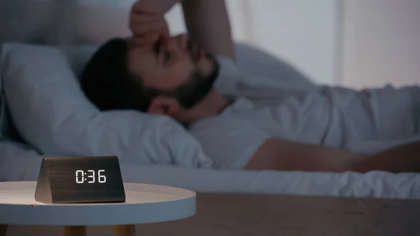 Horloge sur la table de chevet près de l'homme flou dans la chambre à coucher la nuit — Photo de stock