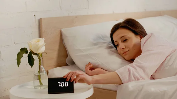 Young woman turning off clock near flower in bedroom — Fotografia de Stock