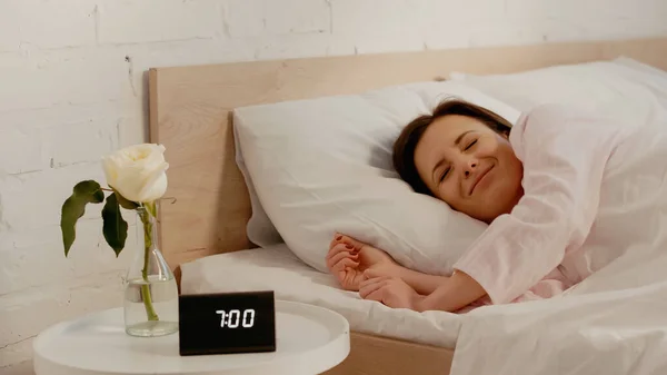 Sleepy woman lying on bed near clock and flower at home — Fotografia de Stock