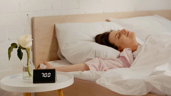 Young brunette woman lying n bed near clock on bedside table — Fotografia de Stock