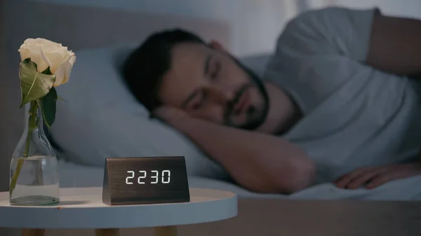 Flower and clock near blurred man sleeping on bed at night — Foto stock