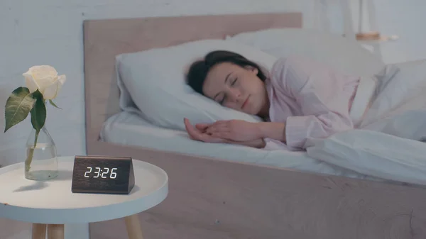 Relógio e planta perto de mulher borrada dormindo na cama à noite — Fotografia de Stock