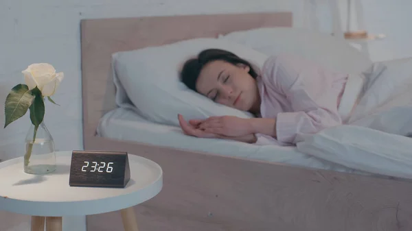 Clock and plant near blurred woman sleeping on bed at night — Fotografia de Stock