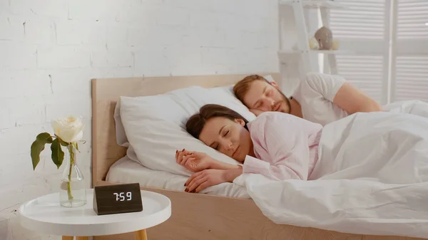 Brunette woman sleeping near clock and husband at home — Fotografia de Stock