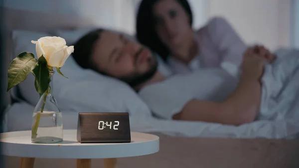Plant and clock near blurred couple on bed at night — Foto stock