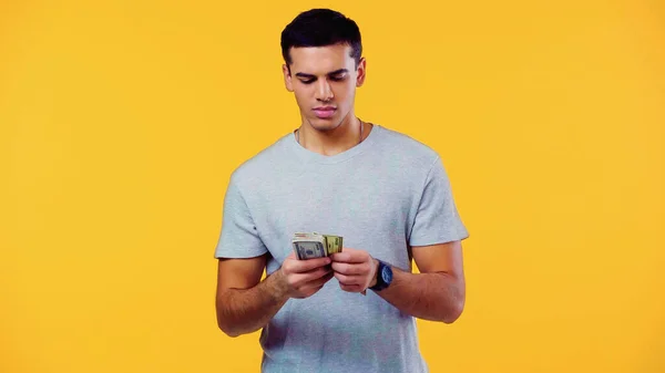 Young man in t-shirt counting dollars isolated on yellow — Fotografia de Stock