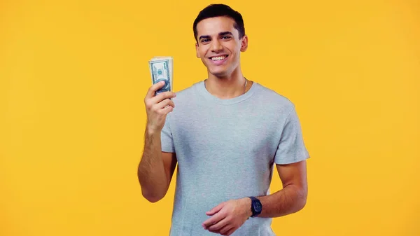 Jovem feliz em t-shirt segurando notas de dólar isolado em amarelo — Fotografia de Stock