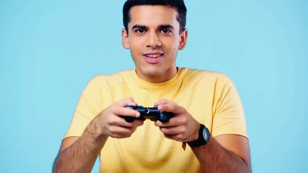 KYIV, UKRAINE - DECEMBER 22, 2021: happy young man holding joystick and playing video game isolated on blue — Stock Photo