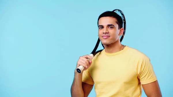 Confident young player in yellow t-shirt holding tennis racket and smiling isolated on blue — Stock Photo