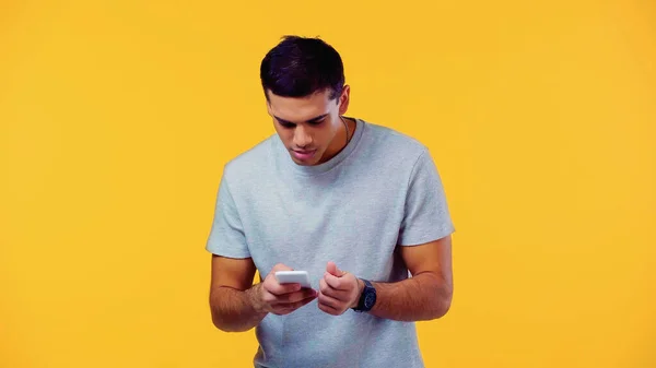 Young man in t-shirt using smartphone isolated on yellow — Stock Photo