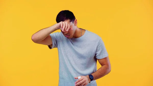 Tired man wiping sweat and holding bottle with water isolated on yellow — Stock Photo