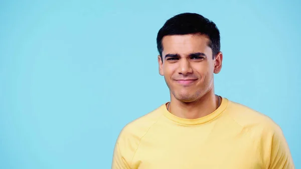 Незадоволений молодий чоловік у жовтій футболці дивиться на камеру ізольовано на синьому — стокове фото
