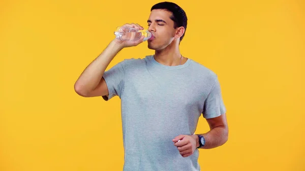 Молодий чоловік із закритими очима п'є воду ізольовано на жовтому — стокове фото