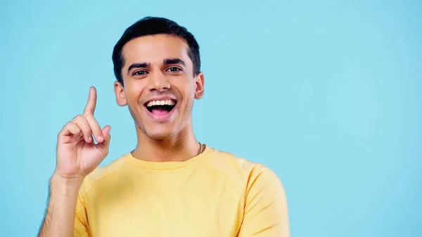 Feliz joven en camiseta amarilla mostrando idea signo aislado en azul - foto de stock