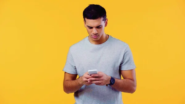 Hombre joven en la mensajería de la camiseta en el teléfono inteligente aislado en amarillo - foto de stock