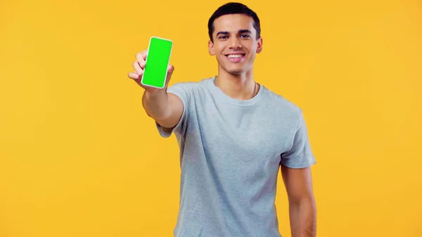 Joven alegre en camiseta que muestra el teléfono inteligente con pantalla verde aislado en amarillo - foto de stock