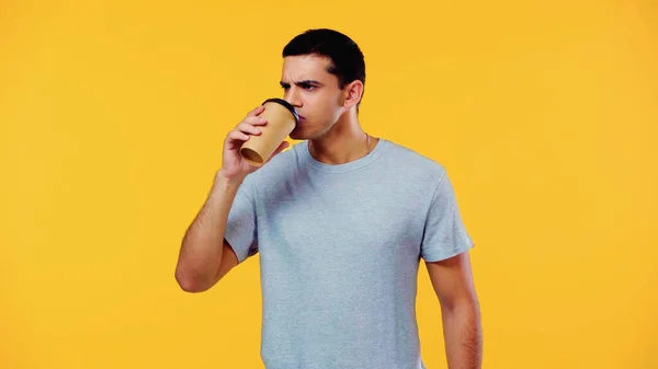 Молодий чоловік у футболці п'є каву, щоб ізольовано на жовтому — стокове фото