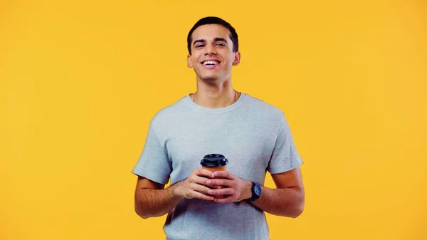 Joven feliz en camiseta sosteniendo taza de papel con café para ir aislado en amarillo - foto de stock