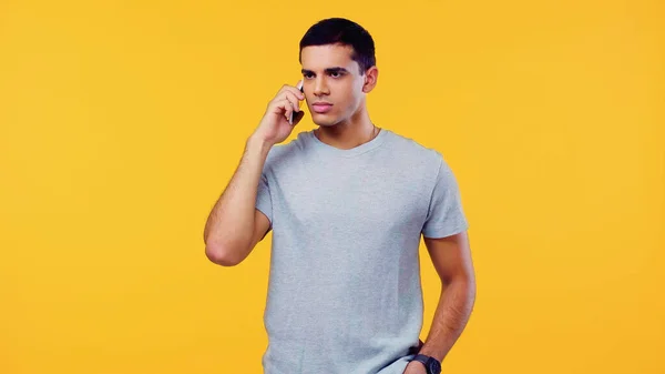 Hombre joven en camiseta hablando en teléfono inteligente aislado en amarillo - foto de stock