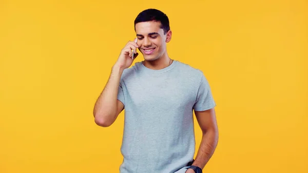 Joven feliz en camiseta hablando en el teléfono móvil aislado en amarillo - foto de stock