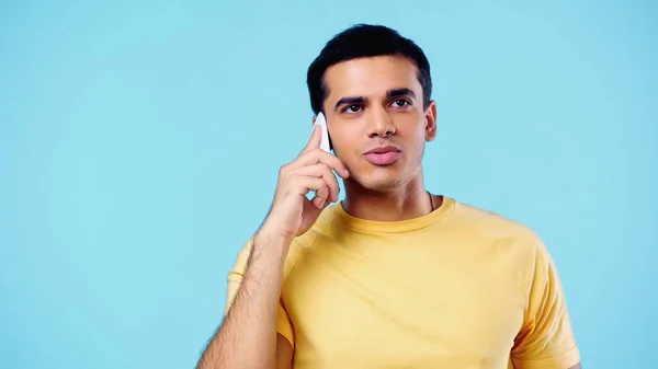 Молодой человек в жёлтой футболке разговаривает по мобильному, изолированному на синий — стоковое фото